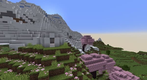 A lone, winding dirt road cuts through a vibrant green field towards distant mountains under a blue sky.